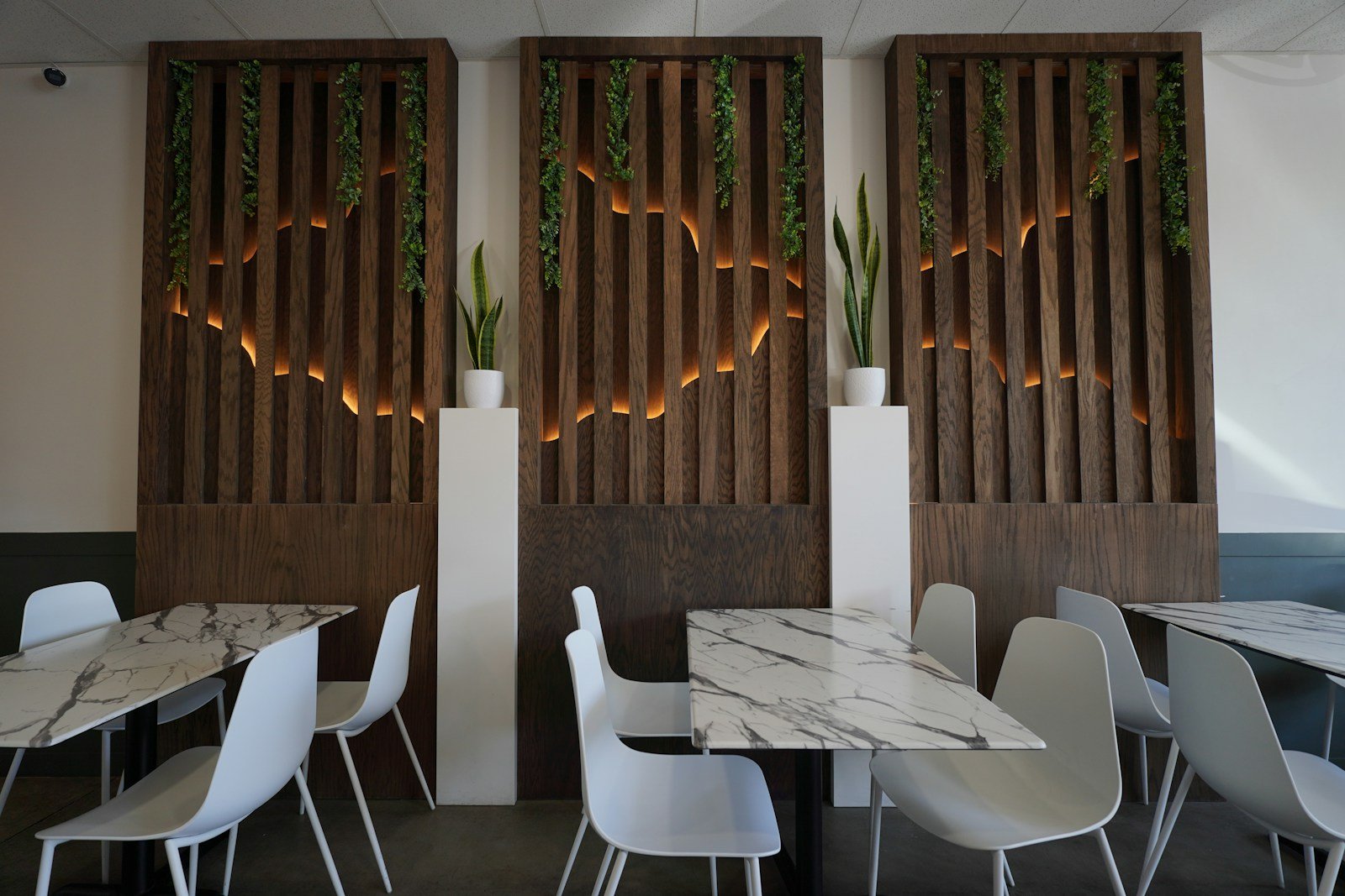 A restaurant with tables and white chairs and wooden screens